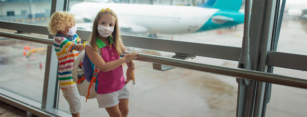 Two children in masks at an airport.